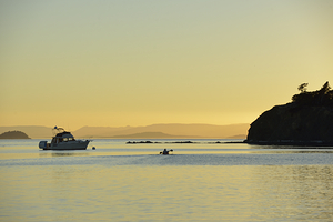 Kayaker and motor boat at anchor in Fox Cove. Sucia Island by Kevin Oke