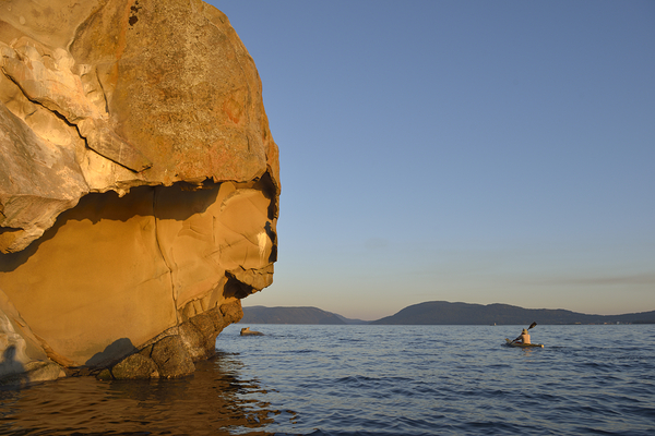 Sea kayaking under sculpted sandstone cliffs Print